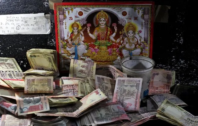 500 and 1000 Indian rupee banknotes are kept in front of an image of the Hindu deities at a cash counter inside a bank in Jammu, November 10, 2016. (Photo by Mukesh Gupta/Reuters)