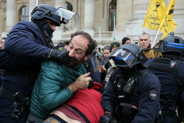 A protester (2nd L) bites the hand of a police officer in riot gear (L) during an action called by the French Farmers' Confederation union (Confederation Paysanne) to protest against the inauguration of the 64th edition of the European Commodities Exchange (Bourse de Commerce Europeenne) at the Grand Palais, in Paris, on December 5, 2024. (Photo by Thomas Samson/AFP Photo)