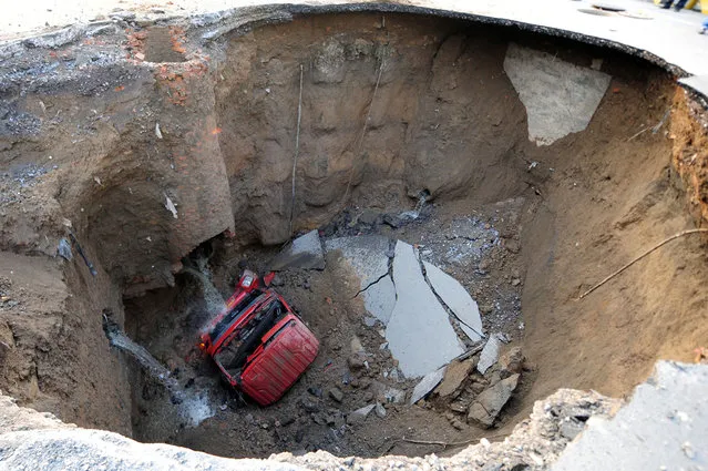 A truck lies in a sinkhole which occurred overnight on Shiliuzhuang road, in Beijing, on April 26, 2011. A section of the road collapsed beneath the truck, slightly injuring the driver and a passenger, who both jumped out the vehicle before it sank into the hole. (Photo by AFP Photo via The Atlantic)