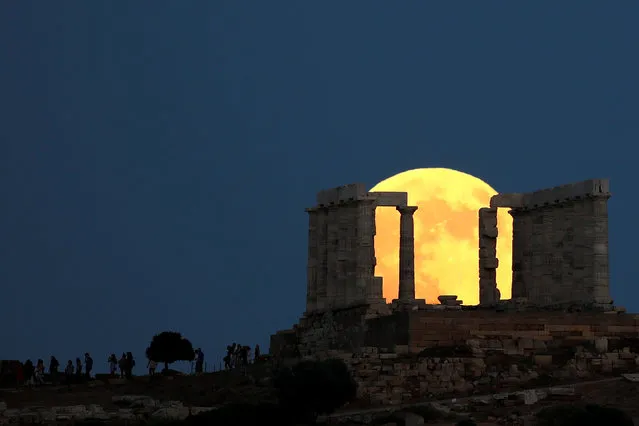People watch a full moon rising behind the Temple of Poseidon before a lunar eclipse in Cape Sounion, near Athens, Greece, July 27, 2018. (Photo by Alkis Konstantinidis/Reuters)
