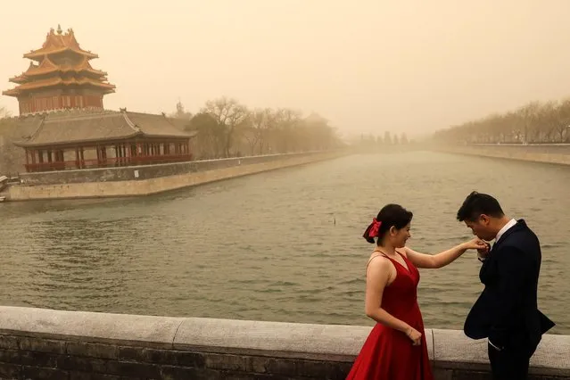 A couple react during their wedding photoshoot near the Forbidden City, as the city is hit by sandstorm, in Beijing, China on March 15, 2021. (Photo by Tingshu Wang/Reuters)