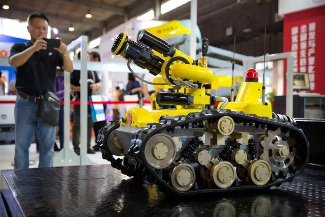 A visitor takes a smartphone photo of a tactical robot from Chinese firm CITIC Heavy Industries at the World Robot Conference in Beijing, China, Wednesday, August 15, 2018. The annual conference is a showcase of China's burgeoning robot industry ranging from companion robots to those deployed on manufacturing assembly line and entertainment. (Photo by Mark Schiefelbein/AP Photo)