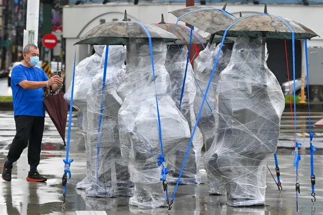 A man takes photographs of sculptures covered in plastic wrap and secured with straps in Keelung on August 3, 2023, as typhoon Khanun approaches the northeastern coast of Taiwan. (Photo by Sam Yeh/AFP Photo)
