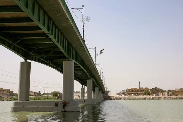 Youths jump into the Euphrates river under the al-Qurnah bridge, north of Basra city in southern Iraq, on June 12, 2023. (Photo by Hussein Faleh/AFP Photo)
