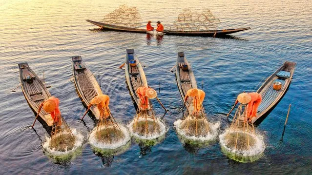 Fishermen are reflected in a lake as they use a traditional technique to catch fish in the shallow waters at sunset. They use conical baskets, also known as traditional Inle fishing nets, to catch carp and tilapia fish on Inle Lake in Myanmar on March 2021. The Intha fishermen wear unique Inle traditional bamboo hats and are known for rowing their boats with their legs. (Photo by Zay Yar Lin/Solent News & Photo Agency)
