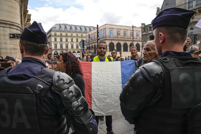 An anti heath pass demonstrator holds a French flag as he faces police officers outside the Constitutional Council in Paris, Thursday, August 5,2021. France's Constitutional Council is deciding on Thursday whether the health pass that is to open the doors and terraces to cafes, restaurants, trains and hospitals starting next week is in line with the nation's most cherished principles. (Photo by Michel Euler/AP Photo)