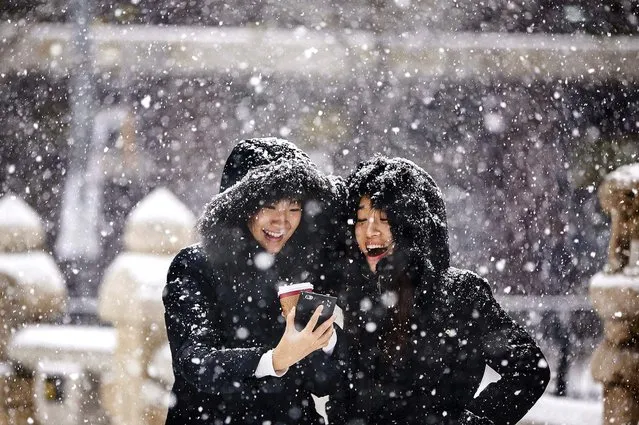 Women smile as they look at a picture on a  phone as it snows in central Seoul, on December 12, 2013. (Photo by Kim Hong-Ji/Reuters)