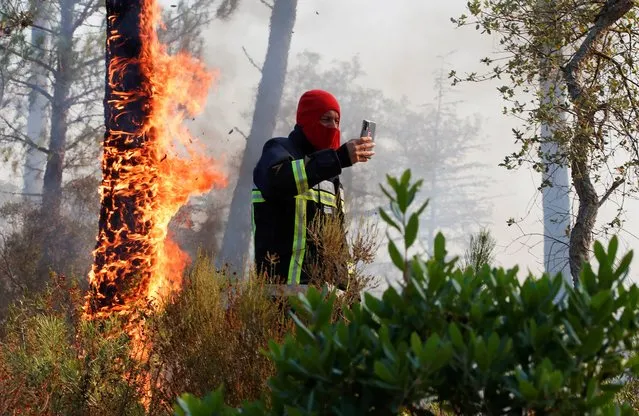 A firefighter takes a picture of a fire during a major wildfire that broke out in Vidauban, in the Var region of southern France, August 18, 2021. (Photo by Eric Gaillard/Reuters)