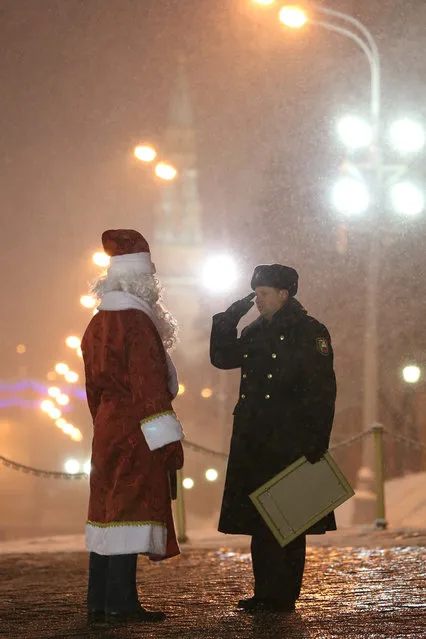 A timber truck driver (L) dressed as Father Frost is saluted by a soldier at the Kremlin's Spasskiye (Saviour) Gate in Moscow, Russian Federation, on December 24, 2013. (Photo by Vyacheslav Prokofyev/ITAR-TASS/ZUMA Press)