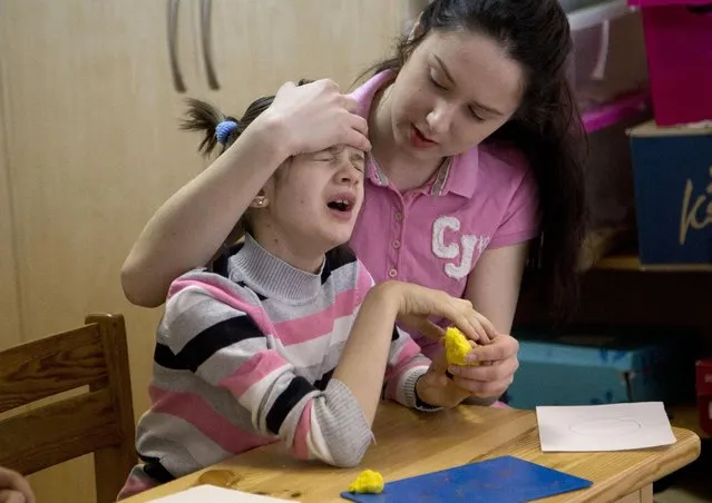 In this photo taken April 14, 2015, Lera, 11, plays with a teacher during an art class in the Center for Children with Disabilities, Rodyna, (Family) in Kiev, Ukraine. International rights group, Disability Rights International said in a report released Thursday April 16, 2015, that growing numbers of disabled children in Ukraine are being condemned to life in orphanages and institutions blighted by neglect and abuse. (Photo by Efrem Lukatsky/AP Photo)