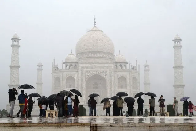 Tourists shelter use umbrellas to shelter from the rain while visiting the Taj Mahal in Agra on November 30, 2023. (Photo by Pawan Sharma/AFP Photo)