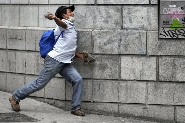 A protester throws a rock at riot police during a protest demanding that a law be passed that compensates veterans for having served during the country's civil war, outside the Congress building in Guatemala City, Tuesday, October 19, 2021. (Photo by Moises Castillo/AP Photo)