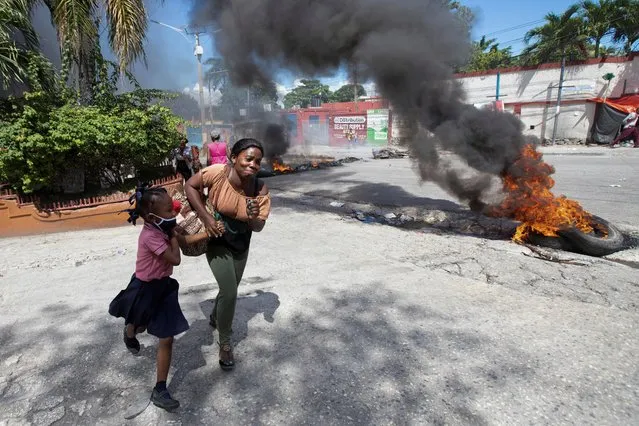 A woman and a girl in a school uniform run past a barricade of burning tires during a demonstration against high prices and fuel shortages, in Port-au-Prince, Haiti on October 21, 2021. (Photo by Ralph Tedy Erol/Reuters)