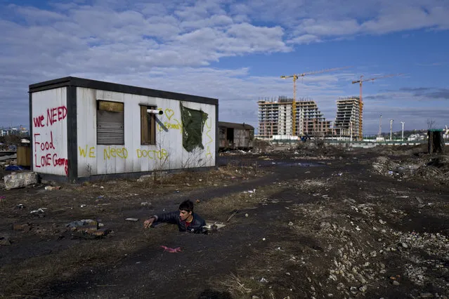 An Afghan refugee youth washes cooking pans in a hole in the ground outside an old train carriage where he and other migrants are taking refuge in Belgrade, Serbia, Sunday, February 5, 2017. Hundreds of migrants have been sleeping rough in freezing conditions in central Belgrade looking for ways to cross the heavily guarded EU borders. (Photo by Muhammed Muheisen/AP Photo)