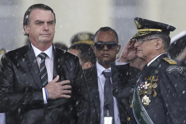 In this April 17, 2019 photo, Brazil's President Jair Bolsonaro puts his hand over his heart as Army Commander Edson Leal Pujol salutes during the playing of the national anthem during a ceremony marking Army Day, in Brasilia, Brazil. Brazil's Army Day is officially on Friday, April 19. (Photo by Eraldo Peres/AP Photo)