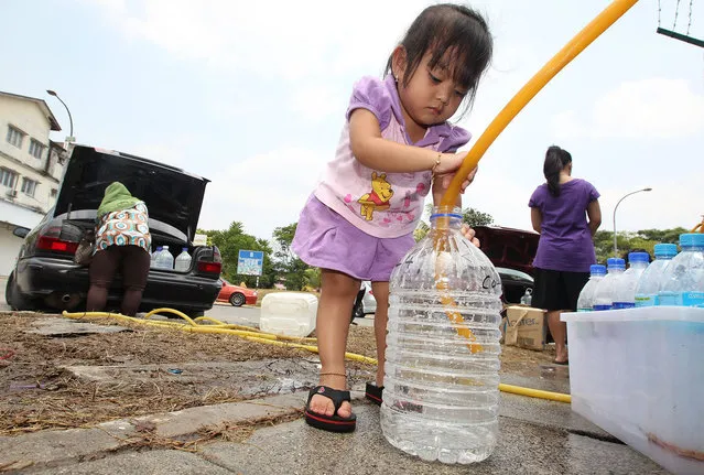 NurNisa Yasmin Mohd Fadzil, 3, the youngest of three siblings, helps her mother, Suhaila Zakaria, 35, fill water into a bottle in Balakong, Selangor, Malaysia on February 26, 2014. (Photo by Norafifi Ehsan/The Star)