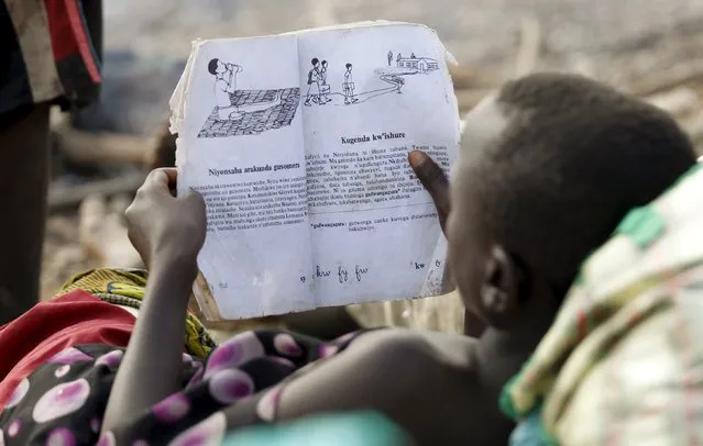A Burundian refugee child reads a book on the shores of Lake Tanganyika in Kagunga village in Kigoma region in western Tanzania, as they wait for MV Liemba to transport them to Kigoma township, May 18, 2015. (Photo by Thomas Mukoya/Reuters)