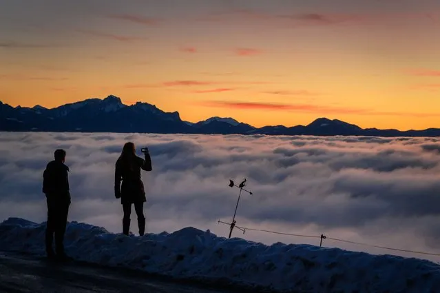A couple is silhouetted with Alps surrounded by a sea of fog hanging above Lake Geneva in Mont de Gourze above Riez, Western Switzerland, after sunset on December 14, 2021. (Photo by Fabrice Coffrini/AFP Photo)