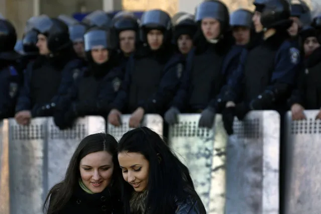 Ukrainian girls look at photos in their mobile phone as riot policemen stand guard in front of the regional administration building in central Donetsk March 22, 2014 during a protest. Several thousands of pro-Russian protesters marched from Lenin square to the regional administration building calling for the return of the pro-Moscow President Yanukovich. (Photo by Yannis Behrakis/Reuters)