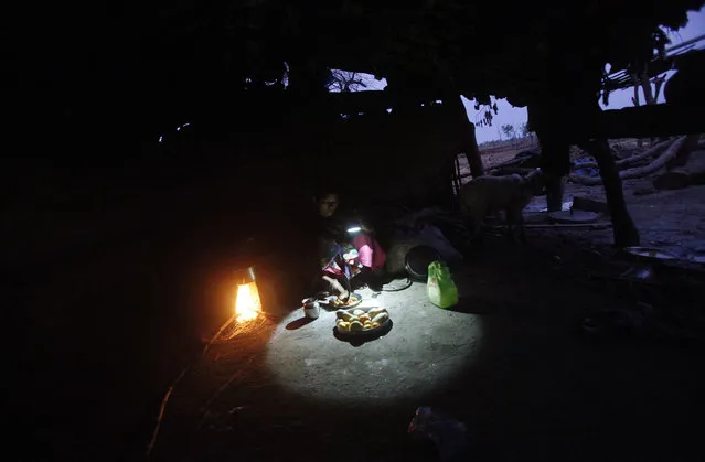 A woman uses a battery operated torch to prepare a meal inside the kitchen of her house at Rampuriya village of Guna district in Madhya Pradesh June 19, 2012. (Photo by Adnan Abidi/Reuters)