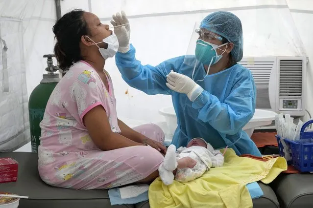 Medical Technologist Erika Alvarado performs a COVID-19 test on a patient who just delivered a baby outside a hospital in Manila, Philippines on Friday, December 24, 2021. In the Philippines, one of the worst-hit by the pandemic in Southeast Asia, daily COVID-19 infections have considerably dropped from an average 22,000 cases just three months ago during an alarming spike set off by the delta variant to just a few hundred in recent days after a delayed vaccination campaign considerably intensified with more vaccine shipment deliveries. (Photo by Aaron Favila/AP Photo)
