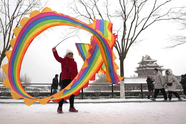 A resident plays a ribbon as visitors walk by the Turret of the Forbidden City covered with snow fall in Beijing, Sunday, February 13, 2022. (Photo by Andy Wong/AP Photo)