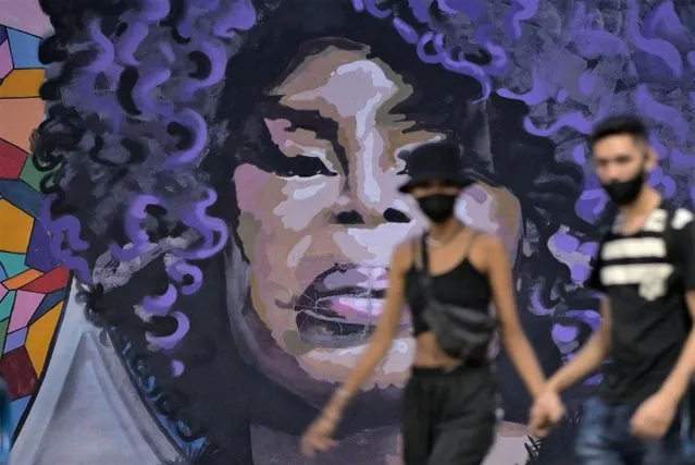 People walk past a mural made by the women’s collective “MINAS DE MINAS CREW”, depicting late Brazilian singer and songwriter Elza Soares, 91, in downtown Belo Horizonte, Minas Gerais state, Brazil on January 20, 2022. Samba singer Elza Soares, often referred to as the Brazilian Tina Turner, died aged 91 in Rio de Janeiro on Thursday, her press office said. (Photo by Douglas Magno/AFP Photo)