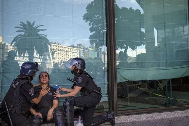 An exhausted police officer is helped by fellow officers during clashes with demonstrators protesting the government agreement with the International Monetary Fund to refinance some $45 billion in debt, as legislators prepare to vote on a law to ratify the agreement, in Buenos Aires, Argentina, Thursday, March 10, 2022. (Photo by Rodrigo Abd/AP Photo)