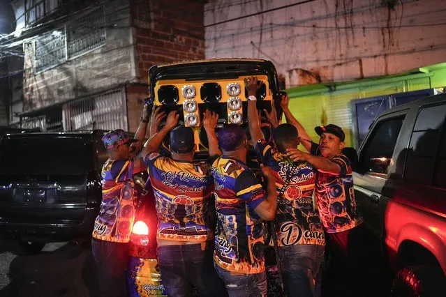 Friends help car owner Luis Daniel Castro, alias Lion, center, raise the lid of his trunk at a mobile party in the Petare neighborhood of Caracas, Venezuela, Friday, March 4, 2022. The trunk of Castro's four-door Hyundai Getz has loudspeakers, amplifiers, bass bins and a space solely meant to show off throughout the night by throwing his shirt in there and having the fabric move to the beat of the music. (Photo by Matias Delacroix/AP Photo)