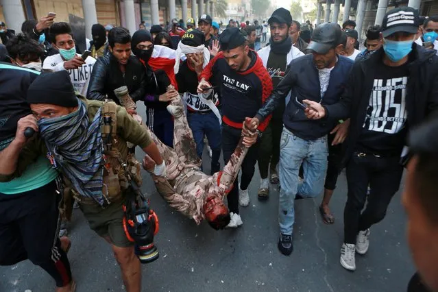 A soldier badly wounded during clashes with anti-government protesters is carried  by demonstrators to a hospital during the ongoing protests in Rasheed Street, Baghdad, Iraq, Tuesday, November 26, 2019. (Photo by Khalid Mohammed/AP Photo)