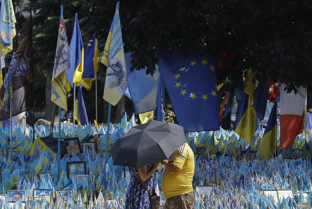 Ukrainians shelter from the sun under an umbrella, in front of Ukrainian national flags set up commemorating fallen Ukrainian soldiers, at Independence Square in Kyiv, Ukraine, 01 July 2024, amid the Russian invasion. Ukrainian president Volodymyr Zelensky confirmed around 31,000 Ukrainian soldiers have been killed since the beginning of the Russian invasion during his press conference on the conflict's second anniversary in February 2024. (Photo by Sergey Dolzhenko/EPA/EFE)