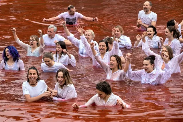 People bathe in a pond, colored red to signify blood, during a protest performance against the Russian invasion of Ukraine in front of the Russian embassy in Vilnius, Lithuania, Thursday, April 7, 2022. Ukrainian officials said the bodies of 410 civilians were found in Kyiv-area towns that were recently retaken from Russian forces. (Photo by Mindaugas Kulbis/AP Photo)