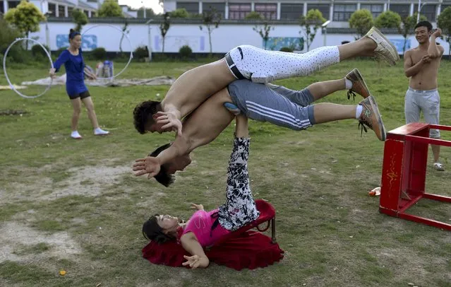 A woman (bottom) balance two men with her feet as students practice at an acrobatic school in Sanwang village, Anhui province, China, July 30, 2015. Over 100 students, mostly young children are currently studying at the school. Most of them came from rural area of Henan, Shandong, Jiangsu and Anhui provinces. Starting at 4 a.m. every morning, students practice an average of 10 hours. The training usually lasts from one month to over a year. (Photo by Reuters/Stringer)