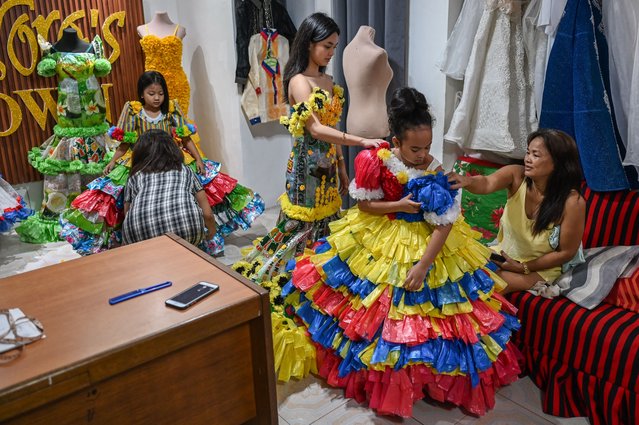 In this photo taken on September 12, 2024, girls try on the dresses made of recycled materials in Cainta, Rizal province. For ten years, Leonora Buenviaje, 53, has been making dresses made from recycled materials as a part of her gown rental business. She incorporates bubble wraps, plastic bags and rice sacks in her designs that people wear during school activities, fashion shows and town festivities (fiesta). She said she wanted children to know that some materials that can be found at home can be repurposed into something beautiful, useful and eco-friendly. (Photo by Jam Sta Rosa/AFP Photo)