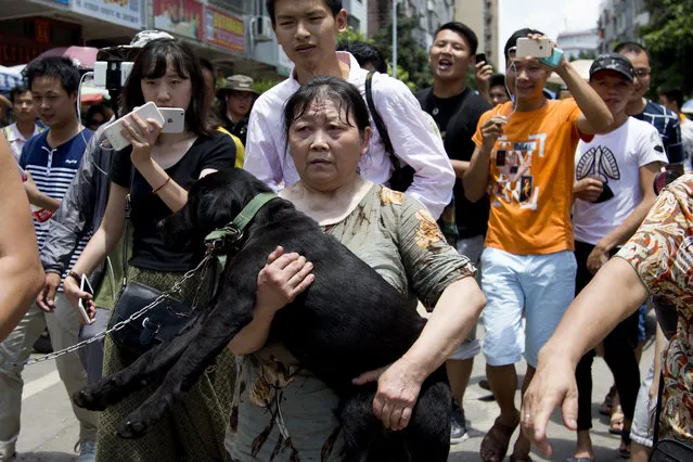 An animal rights activist, center, carries a dog which she bought as she leaves a market after being confronted by dog sellers and people during a dog meat festival in Yulin in south China's Guangxi Zhuang Autonomous Region, Tuesday, June 21, 2016. (Photo by Andy Wong/AP Photo)