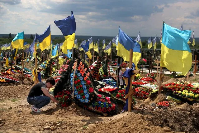 A woman reacts next to a grave of Evgeny Khrapko, a combat medic and instructor of tactical medicine who was killed in a mission, amid Russia's attack on Ukraine, after his farewell ceremony in Kharkiv, Ukraine June 14, 2022. (Photo by Ivan Alvarado/Reuters)