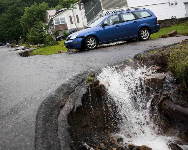 Water rushes past a damaged car and into a chasm of exposed piping created by flood damage on Oarkford Avenue in Richwood, W.Va. on Friday June 24, 2016. (Photo by Christian Tyler Randolph/Charleston Gazette-Mail via AP Photo)