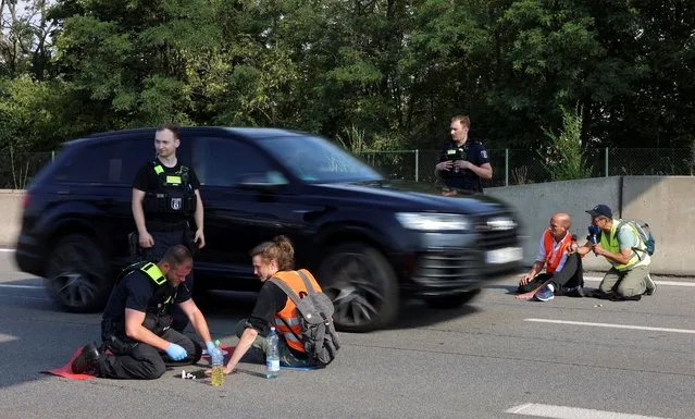 A police officer removes a “Letzte Generation” (Last Generation) activist that glued his hand to the road, as they block a highway under the slogan “Let's stop the fossil madness!” for an end to fossil fuels and against oil drilling in the North Sea, in Berlin, Germany on July 4, 2022. (Photo by Christian Mang/Reuters)