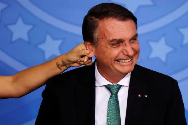Brazil's President Jair Bolsonaro reacts as his ear is pulled by first lady Michelle Bolsonaro during a ceremony by the National Program of Civic-Military Schools, at the Planalto Palace in Brasilia, Brazil on November 24, 2021. (Photo by Ueslei Marcelino/Reuters)