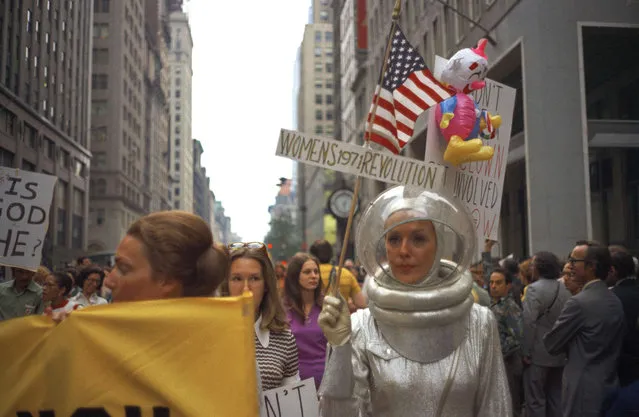 A woman dressed in an alien space suit carries an American flag and a sign that reads “Women's Revolution 1971” as she marches in a Women's Liberation demonstration on Fifth Avenue in New York, August 26, 1971. (Photo by Marty Lederhandler/AP Photo)