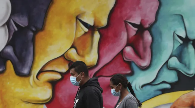 Pedestrians, wearing protective face masks as a precaution against the spread of the new coronavirus, walk past a mural in Quito, Ecuador, Saturday, March 28, 2020. The government has declared a health emergency, enacting a curfew and restricting movement to only those who provide basic services. (Photo by Dolores Ochoa/AP Photo)