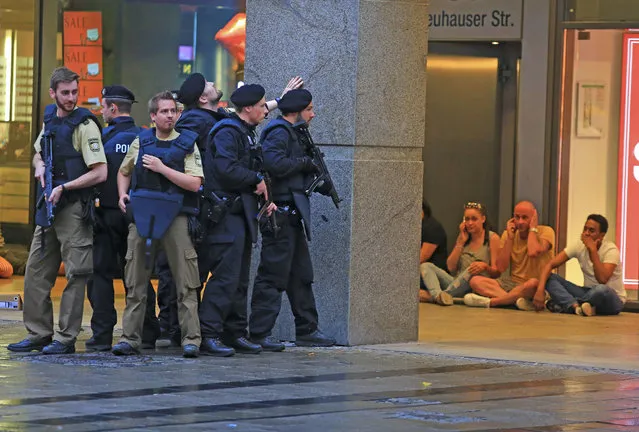 In this Friday, July 22, 2016 photo provided by Wael Ladki people take shelter as armed police officers are on the hunt for possible fugitives after a shooting in a shopping mall in Munich, southern Germany. A gunman killed 9 people before killing himself. (Photo by Wael Ladki via AP Photo)