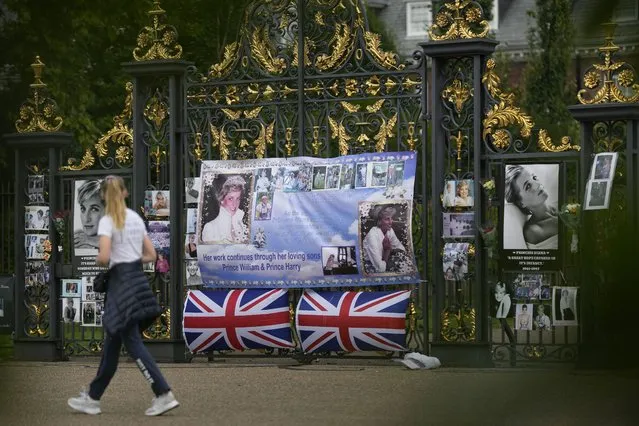 A woman walks by portraits of Princess Diana displayed on the gates of Kensington Palace, in London, Tuesday, August 30, 2022. This week marks the 25th anniversary of Princess Diana's death in a Paris car crash. (Photo by Alastair Grant/AP Photo)