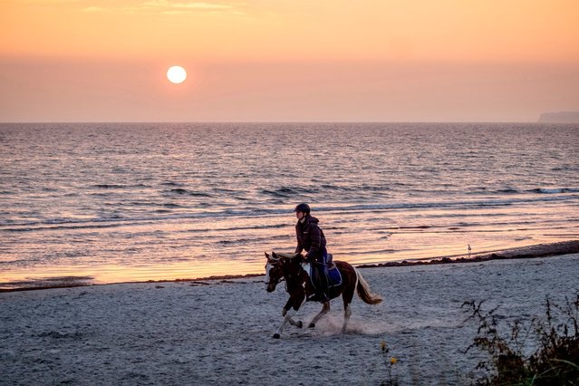 A young woman rides her horse along the Baltic Sea in Haffkrug, northern Germany, as the sun rises on Friday, October 25, 2024. (Photo by Michael Probst/AP Photo)