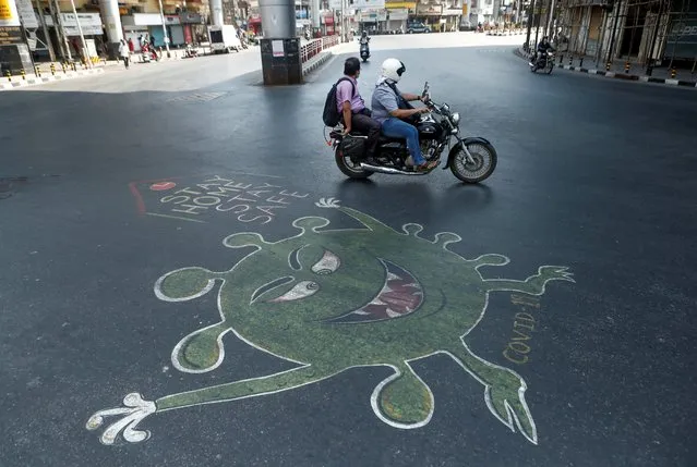 People ride past a graffiti on a road depicting the coronavirus, as an attempt to raise awareness about the importance of staying at home during a nationwide lockdown to slow the spreading of the coronavirus disease (COVID-19), in Mumbai, April 20, 2020. (Photo by Francis Mascarenhas/Reuters)
