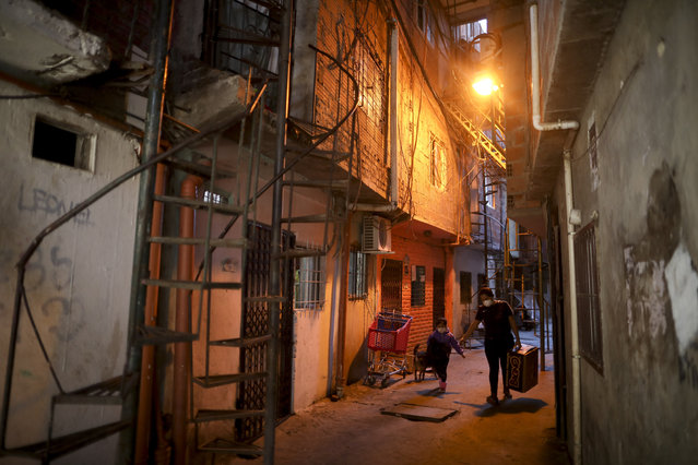 A woman and a child, wearing protective face masks to help curb the spread of the new coronavirus, walk through an alley in the Villa 31 slum during a government-ordered shutdown, in Buenos Aires, Argentina, Thursday, April 30, 2020. According to official data, the number of confirmed cases of COVID-19 in the city's slum have increased in the past week, putting authorities on high alert. (Photo by Natacha Pisarenko/AP Photo)
