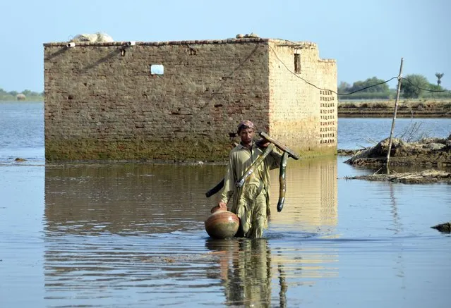 A man carries some belongings as he wades through floodwaters in Jaffarabad, a flood-hit district of Baluchistan province, Pakistan, Monday, September 19, 2022. Pakistan said Monday there have been no fatalities for the past three days from the deadly floods that engulfed the country since mid-June, a hopeful sign that the nation is turning a corner on the disaster. (Photo by Zahid Hussain/AP Photo)