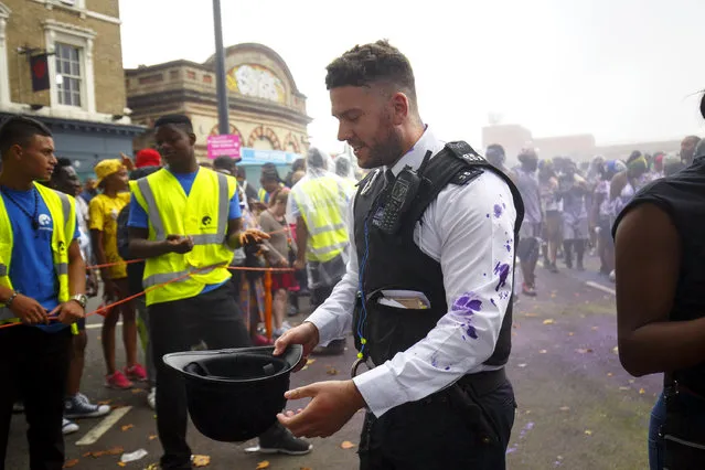 A police officer reacts after getting hit by paint whilst dancers and children parading on family day of Notting Hill Carnival in west London, Sunday, 28 August 2016. (Photo by Tolga Akmen/London News Pictures)
