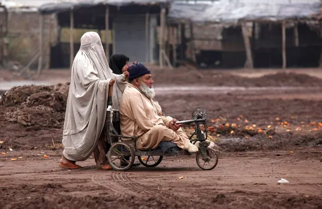 A family helps a disabled man with his wheelchair on a roadside outside Peshawar, Pakistan on February 2, 2017. (Photo by Fayaz Aziz/Reuters)