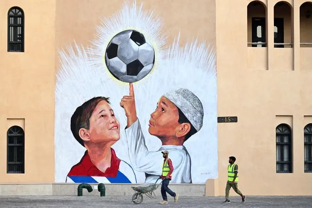 A worker pushes a wheelbarrow past a mural in Doha on November 8, 2022, ahead of the Qatar 2022 FIFA World Cup football tournament. (Photo by Gabriel Bouys/AFP Photo)